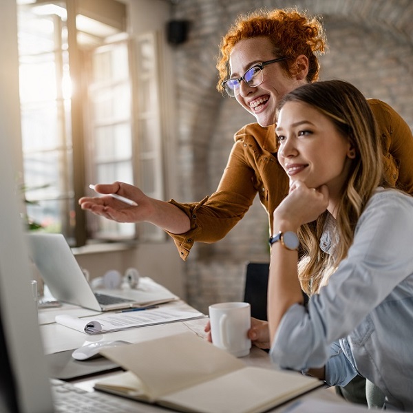 Young happy businesswomen cooperating while using desktop PC in the office.